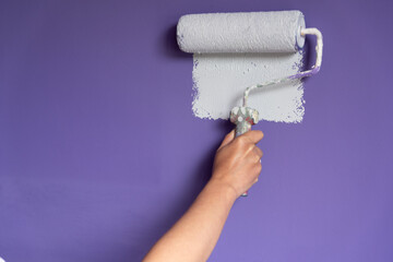 Woman hand applying light color paint to wall with roller
