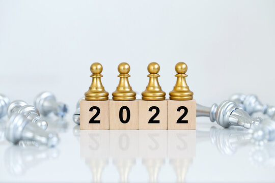Golden chess pieces are placed on wooden blocks with numbers 2022 surrounding them with silver chess pieces. Concept to start the new year with victory