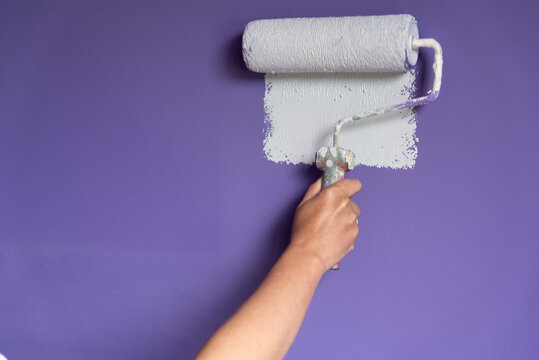 Woman hand applying light color paint to wall with roller