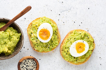 Toast with mashed avocado and egg topped with sesame seeds on grey concrete background top view