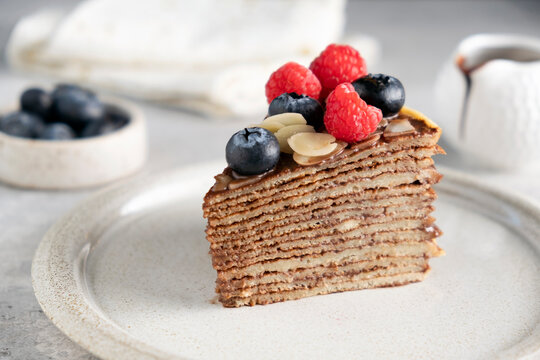 Slice of chocolate crepe cake with berries on a plate