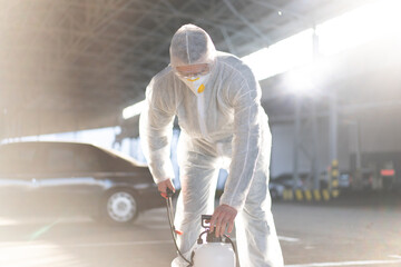 Man dressed white protective overalls spraying surface antibacterial sanitizer sprayer during quarantine