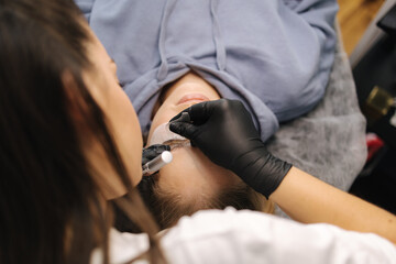 Woman doing eyelashes lamination in beauty studio. Blond hair model has staining, curling, laminating and extension for lashes