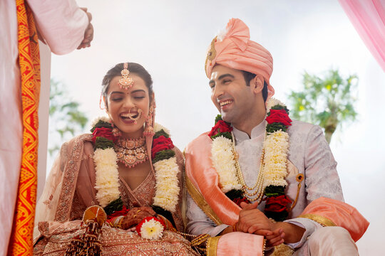 Happy Indian bride and groom sitting together at wedding mandap