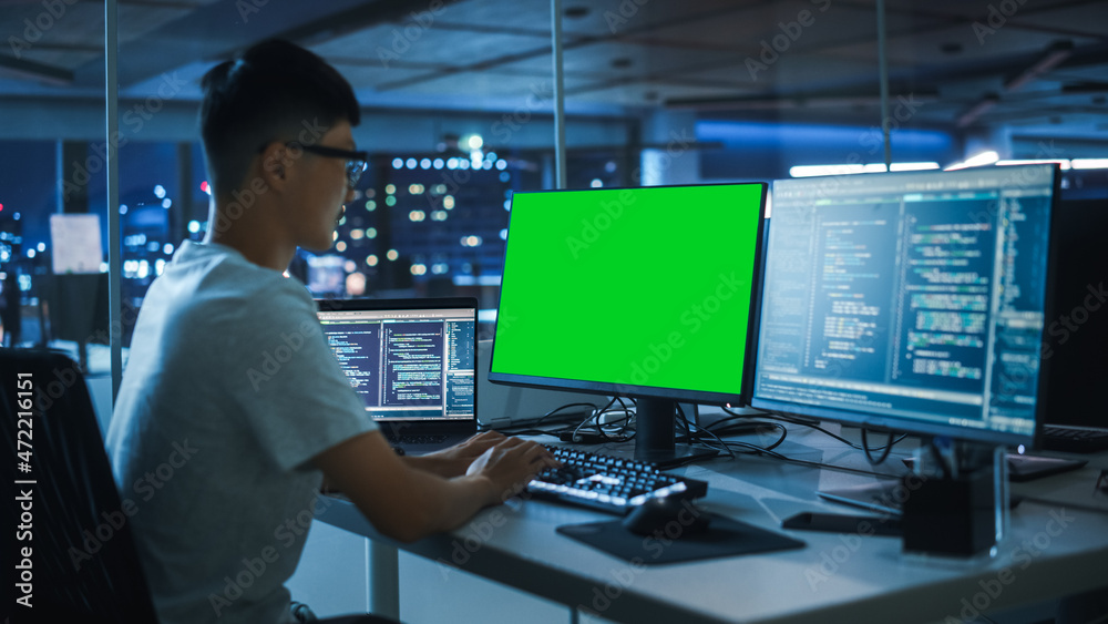 Poster Night Office: Young Japanese Man in Working on Green Screen Chroma Key Desktop Computer. Programmer Typing Code, Creating Modern Software, e-Commerce App Design. Over Shoulder