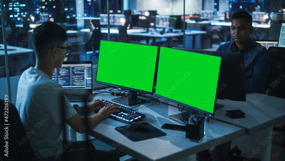 Poster Night Office: Young Japanese Man in Working on Green Screen Chroma Key Desktop Computer. Team of Programmers Typing Code, Creating Modern Software, e-Commerce App Design, e-Business Programming