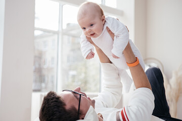 Father laying on the bed with his little infant baby. Family together at home. Single dad. Parental...