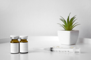Cosmetic bottle for injection on the background of a syringe and a green flower.