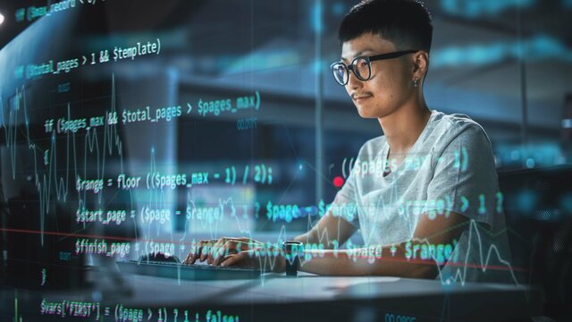 Shot with Visualisation of Running Script Code on Foreground. Young Japanese Man Working on Desktop Computer at Night Office. Digital Entrepreneur Creating Modern Software, e-Commerce App Design.