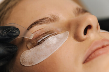 Close-up of eyelash care treatment procedures. Beautiful female, blond hair model have eyelashes lamination. Woman doing staining, curling, laminating and extension for lashes