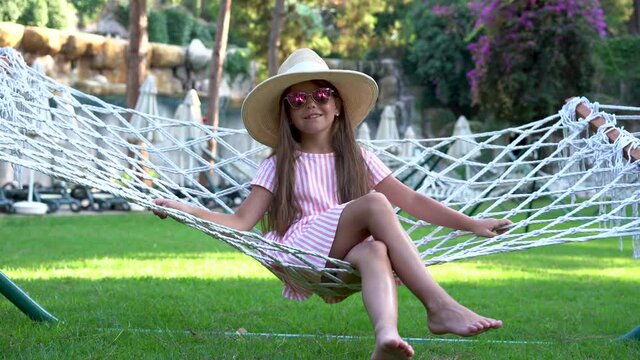 Happy beach vacation little girl relaxing lying down on outdoor patio hammock tanning smiling happy sunbathing during summer holidays. Children on tropical vacations