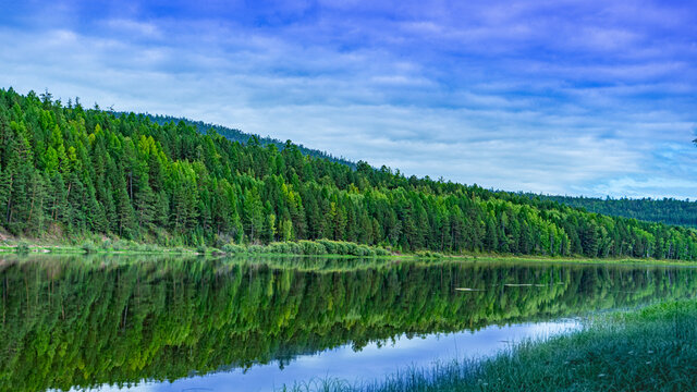 Landscape of the river bank in Siberia. bright juicy colors hilly riverbank and blue clouds
