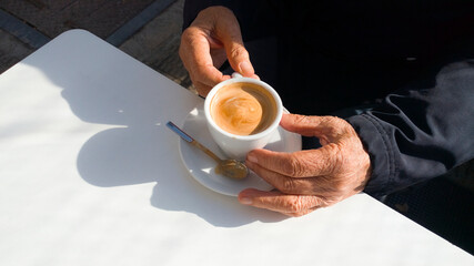 an older man has a cup of coffe  latte at a white table
