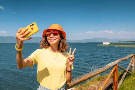 Girl travel blogger takes selfies for her social networks on a background of a picturesque Sevan Lake in Armenia