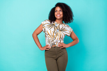 Photo of confident dreamy dark skin lady wear print t-shirt smiling arms waist looking empty space isolated turquoise color background