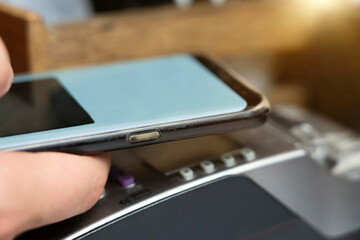 Man pays via payment terminal and mobile phone in cafe. Closeup hand of man holding a mobile phone and paying at the POS terminal. Soft selective focus