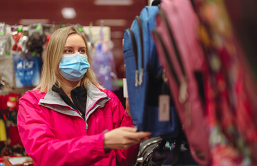 Woman in medical mask is choosing kid backpack for school.