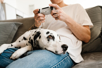 Young man with dog sitting on sofa and holding joystick