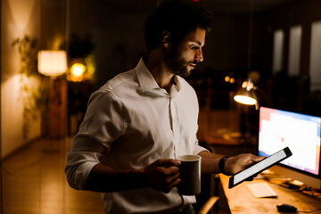 White bearded man drinking coffee while working with tablet computer