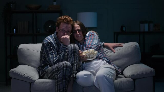 Couple on a sofa at night watching a scary movie