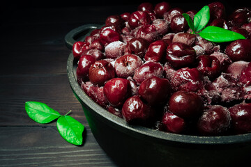 A lot of frozen cherry without sticks and green leaves on a wooden black background.Vitamins and a healthy diet