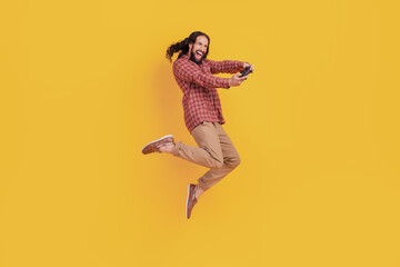 Photo of positive gamer man hold gamepad enjoy videogame wear checkered shirt isolated on yellow color background © Tetiana