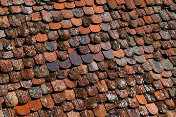 Traditional red clay roof tiles in Rothenburg ob der Tauber, a medieaval historic town in Franconia Bavaria Germany. Wheathered old surface with shades of grey, orange and brown in irregular rows.