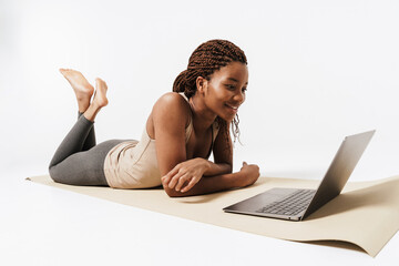 Young black woman using laptop during yoga practice on mat