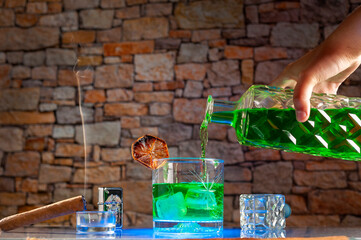 glass of green liquor with ice and an old bottle of green drink and cigar making smoke