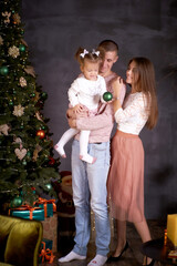 Young happy family with little baby girl in cozy home interior with festive Christmas tree. Good mood and having fun together. Merry Christmas concept. Happy parenthood