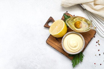 a bowl of mayonnaise with corolla, napkin, lemon, oil on the wooden grey background. Copy space....