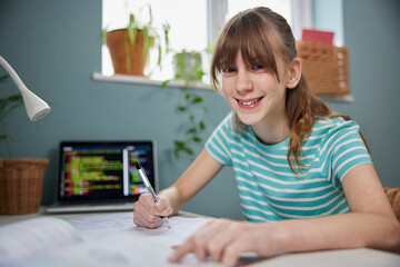 Portrait Of Teenage Girl Doing Homework At Desk In Bedroom