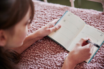 Teenage Girl Lying On Bed At Home Writing Resolutions In New Year 2022 Diary