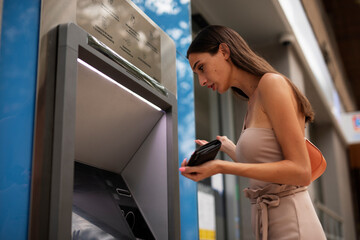 Fototapeta na wymiar Pretty brunette woman withdraving cash. Young woman using ATM machine