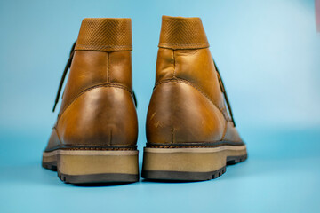 New pair of winter leather boots on a light blue background. Back view of the heels. Fashionable concept.