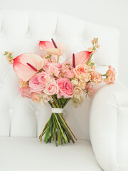 Bridal bouquet with pink roses and anthurium flowers on white armchair. Traditional floral composition for bride on wedding ceremony.
