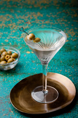 Dirty martini cocktail in martini glass with olives garnish on green colored table