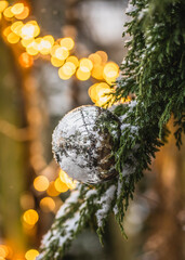 Close-up of one big silver Christmas ball on a snow-covered fir branch, festive atmosphere, selective focus.