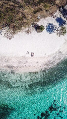 A drone shot of couple lying on a beach on a paradise island in Komodo National Park, Flores, Indonesia. Brownish island turns into white sand beach and further into green and navy sea. Honeymooners