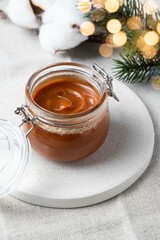 Homemade salted caramel sauce in glass jar on grey background. Cristmas or New year concept. Bakery present, pastry gift. Selective focus.