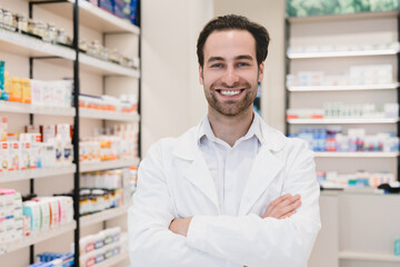 Fototapeta na wymiar Closeup photo of male caucasian confident successful young pharmacist druggist in white medical coat standing with arms crossed at the cash point desk in pharmacy drugstore