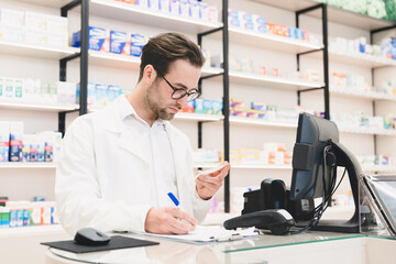 Caucasian male young pharmacist druggist in white medical coat writing from prescription side...