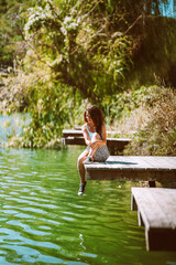 A charming young woman in a skirt is sitting on a wooden bridge against the background of nature with a lake in the forest. Travel, freedom, the concept of an active lifestyle.
