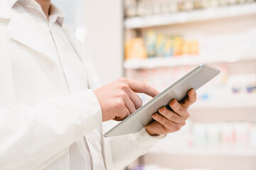 Closeup cropped image of druggist pharmacist using digital tablet for checking expiration date,...