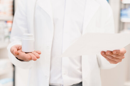 Closeup cropped image of druggist pharmacist looking reading prescription for checking expiration date, side effects, active substance of drugs, pills, medicines in pharmacy