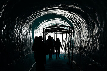 Inside a glacier in the Alps - a cave tunnel inside the ice with the silhouettes of people walking...