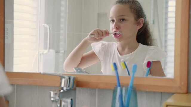 Portrait happy cute young teenage girl brushing teeth in bathroom and smiling. Children daily healthcare routine. Caucasian kid with white tooth looking at mirror isolated at home. Lifestyle.