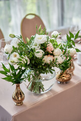 Beautiful floral arrangement of rose flowers and greenery on wedding table in restaurant, copy space. Luxury wedding decorations. Table setting