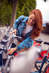 Fototapeta na wymiar Young Woman Hiring Bike As Green Form Of Transport To Get Around City