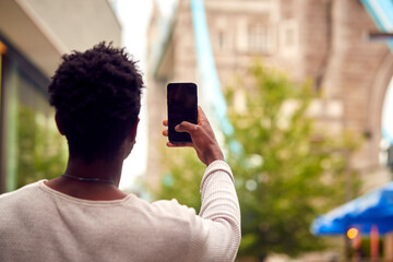Fototapeta na wymiar Male Vlogger Or Social Influencer In London Taking Photo On Mobile Phone Of Tower Bridge